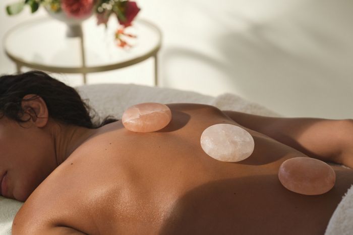 Woman laying on massage bed with 3 marble stone on her back